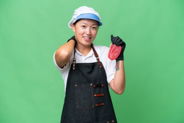 Young caucasian woman wearing an apron and serving fresh cut meat over isolated background laughing