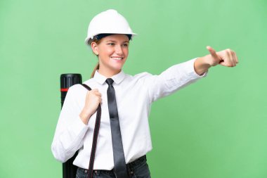 Miğferli, kafkasyalı genç bir kadın izole edilmiş arka plan üzerinde elinde planlar tutarak baş parmak işareti yapıyor.