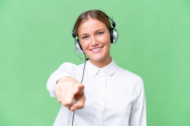 Telemarketer caucasian woman working with a headset over isolated background points finger at you with a confident expression