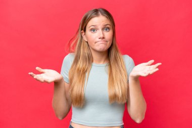 Genç ve güzel bir kadın, kırmızı arka planda izole edilmiş, ellerini kaldırırken şüphe içinde.