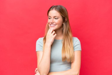 Kırmızı arka planda izole edilmiş genç ve güzel bir kadın. Yan tarafa bakıyor ve gülümsüyor.