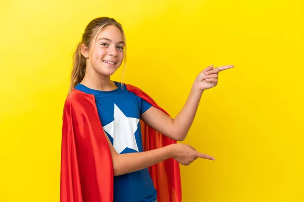 スーパーヒーロー女の子孤立した上に黄色の背景指差し指に側と製品を提示 — ストック写真