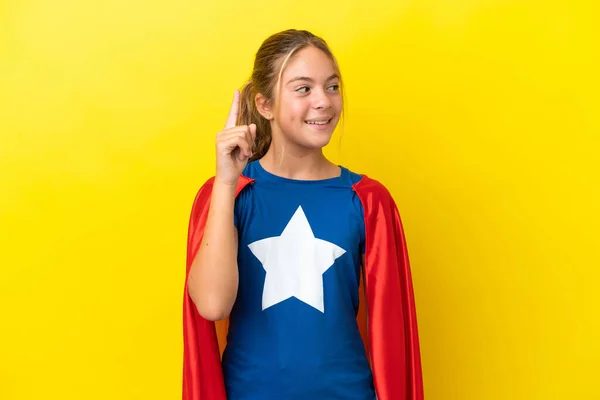 指を持ち上げながら解決策を実現しようとして黄色の背景に隔離されたスーパーヒーローの女の子 — ストック写真