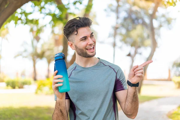 stock image Young handsome sport man with a bottle of water at outdoors pointing to the side to present a product