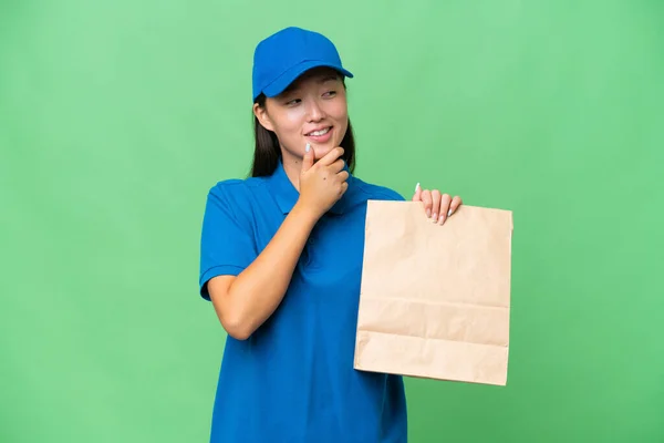 年轻的亚洲女人拿着一袋外卖食品 背景偏僻 朝旁边看去 面带微笑 — 图库照片