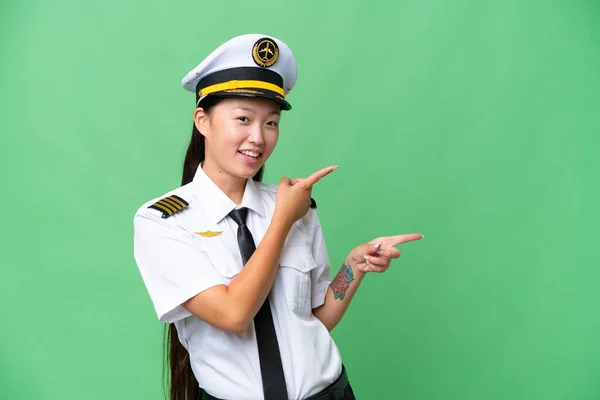 비행기 조종사인 아시아 여자가 배경을 가리키면서 손가락으로 가리키면서 제품을 제공하는 — 스톡 사진