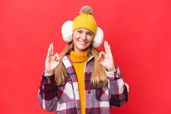 年轻美丽的女人穿着冬衣 红底孤立 手指头上有个好的标志 — 图库照片