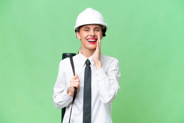 Young architect woman with helmet and holding blueprints over isolated background shouting with mouth wide open