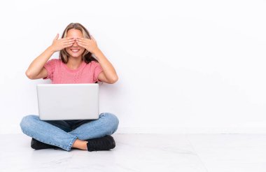 Yerde dizüstü bilgisayarı olan genç bir Rus kız. Beyaz arka planda izole edilmiş. Gözlerini elleriyle kapatıyor.
