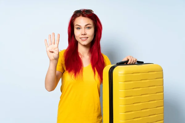 旅行的女孩拿着一个蓝色背景的手提箱 高兴极了 她用手指数着四个 — 图库照片