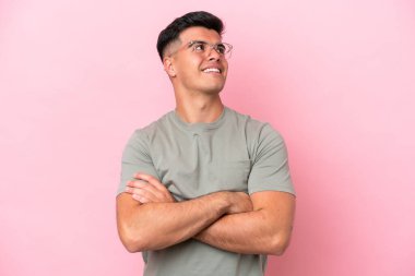 Beyaz tenli yakışıklı adam pembe arka planda izole edilmiş gülümserken yukarı bakıyor.