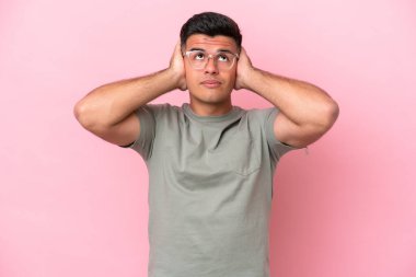 Pembe arka planda izole edilmiş genç beyaz yakışıklı adam hayal kırıklığına uğramış ve kulaklarını kapatmış.