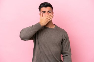 Beyaz tenli yakışıklı bir adam pembe arka planda izole edilmiş. Ağzını eliyle kapatıyor.