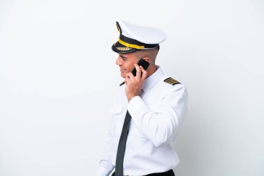 Beyaz arka planda izole edilmiş beyaz bir uçak pilotu cep telefonuyla biriyle sohbet ediyor.