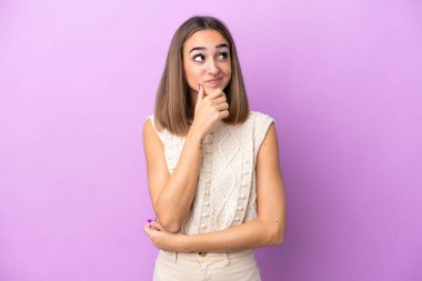 Kafkasyalı genç bir kadın mor arka planda izole edilmiş bir şekilde yukarı bakarken bir fikir düşünüyor.