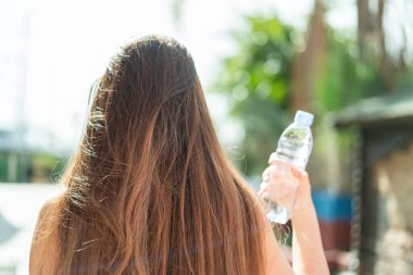 Arka tarafta elinde bir şişe su olan güzel beyaz bir kadın var.