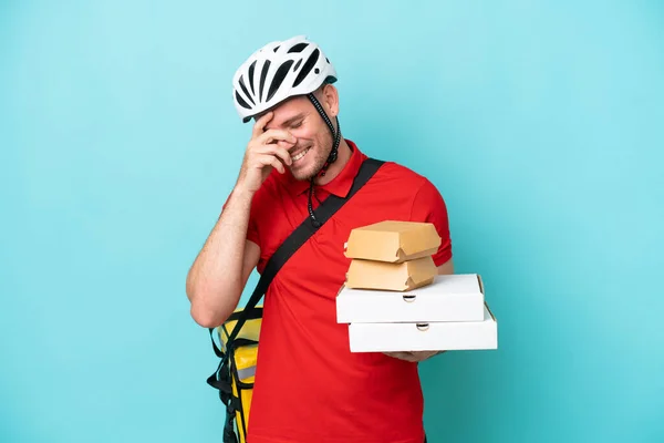 stock image Young caucasian man with thermal backpack and holding fast food isolated on blue background laughing
