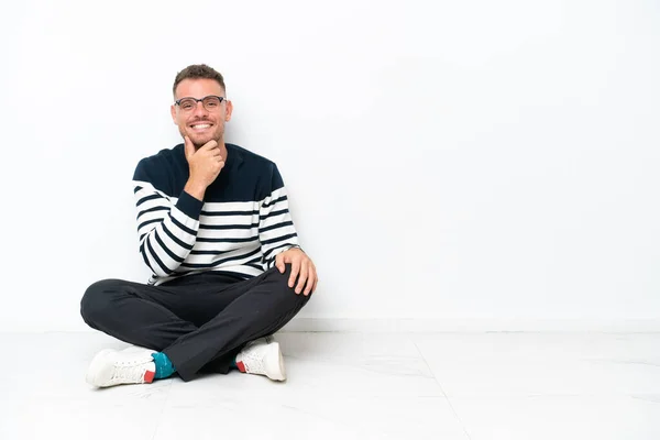 Mladý Muž Sedí Podlaze Izolované Bílém Pozadí Brýlemi Usmívá — Stock fotografie
