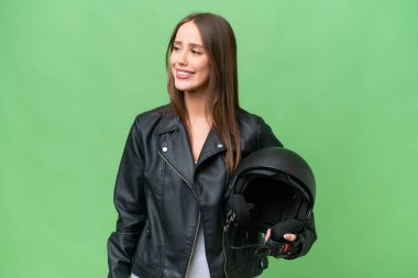 Motosiklet kasklı, izole edilmiş arka planda genç, beyaz bir kadın yana bakıyor ve gülümsüyor.