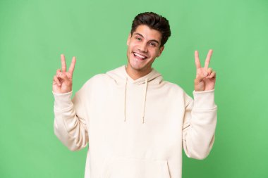 İzole edilmiş arka planda genç beyaz yakışıklı adam iki eliyle zafer işareti gösteriyor.