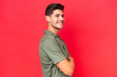 Kızıl arka planda izole edilmiş, kolları bağlı ve mutlu, beyaz, yakışıklı bir genç.