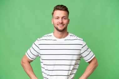 Sarışın, beyaz, soyutlanmış, kalçasında kollarıyla poz veren ve gülümseyen bir adam.