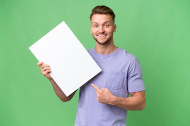 Sarışın, beyaz bir adam izole edilmiş bir zeminde elinde mutlu bir ifadeyle boş bir levha tutuyor ve onu işaret ediyor.