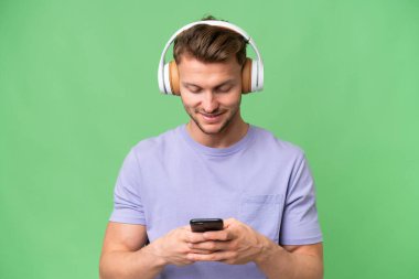 Sarışın, beyaz bir adam izole edilmiş arka planda müzik dinliyor ve cep telefonu arıyor.
