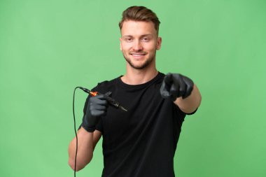 Dövme sanatçısı beyaz adam izole arka planda mutlu bir ifadeyle ön tarafı işaret ediyor