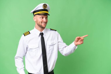 Uçak pilotu izole edilmiş arka planda parmak göstererek bir ürün sunuyor.