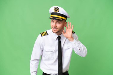 Uçak pilotu, arka planda izole edilmiş bir şekilde elini kulağına koyarak bir şey dinliyor.