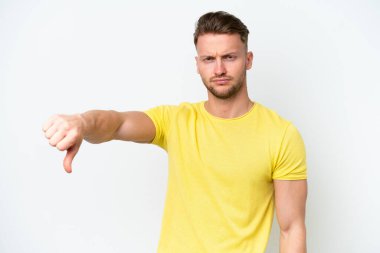 Beyaz arka planda izole edilmiş genç, sarışın beyaz bir adam, olumsuz bir ifadeyle baş parmağını aşağı gösteriyor.