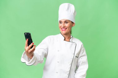 Orta yaşlı aşçı kadın izole bir arka planda selfie çekiyor.