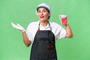 Kasap kadın önlük takıyor ve soyutlanmış arka planda taze et servis ediyor.