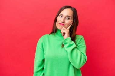 Orta yaşlı beyaz kadın kırmızı arka planda izole edilmiş ve düşünüyor.