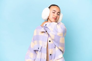 Kış manşeti takan genç bir Arap kadın mavi arka planda izole edilmiş, omuz ağrısından muzdarip, gayret gösterdiği için.