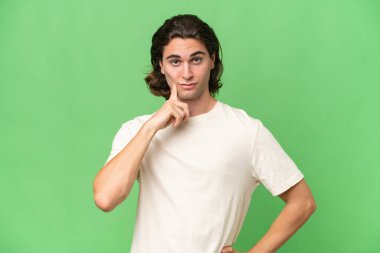 Genç beyaz adam yeşil krom arka planda izole edilmiş ve düşünüyor.