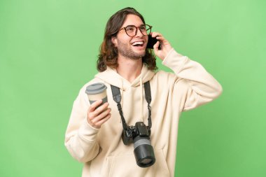 İzole edilmiş arka planda genç bir fotoğrafçı elinde kahve ve bir cep telefonu tutuyor.