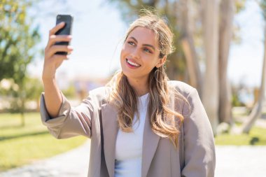 Genç, güzel sarışın Uruguaylı kadın açık havada selfie çekiyor.