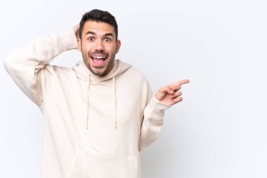 Beyaz arka planda izole edilmiş genç, beyaz bir adam şaşırmış ve parmağıyla kenarı işaret ediyor.
