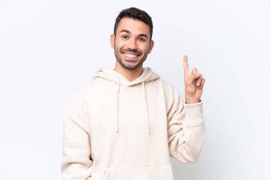 Beyaz arka planda izole edilmiş genç beyaz bir adam en iyinin işareti olarak parmağını kaldırıyor.