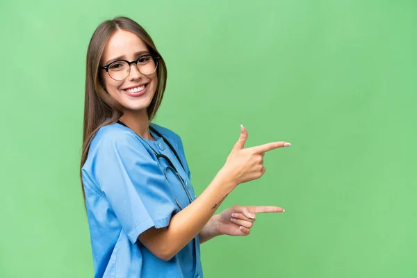 孤立した背景を持つ若い看護師の白人女性が指を横に向けて製品を提示 — ストック写真