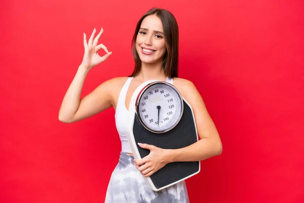 Young Beautiful Caucasian Woman Isolated Red Background Holding Weighing Machine — Stock Photo, Image