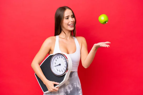 Young Beautiful Caucasian Woman Isolated Red Background Weighing Machine Apple — Stock Fotó
