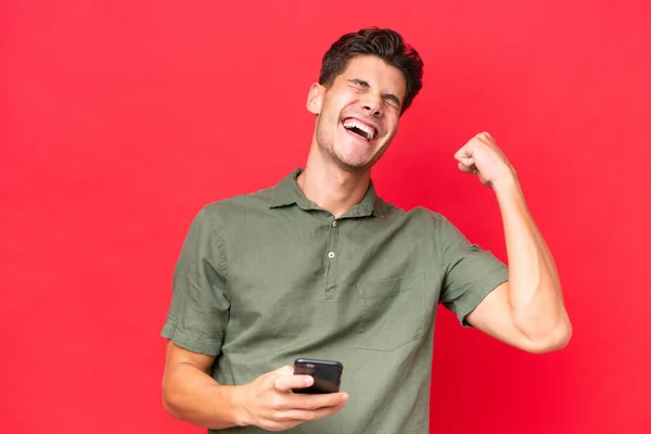 Young Caucasian Handsome Man Isolated Red Background Phone Victory Position — Stock Photo, Image