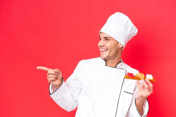 Giovane Chef Caucasico Uomo Tenendo Sashimi Isolato Sfondo Rosso Puntando — Foto Stock