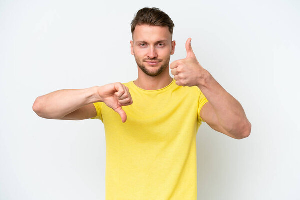 Young blonde caucasian man isolated on white background making good-bad sign. Undecided between yes or not