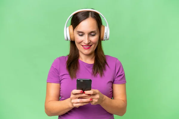 Middle Aged Caucasian Woman Isolated Background Listening Music Looking Mobile — Stock Photo, Image