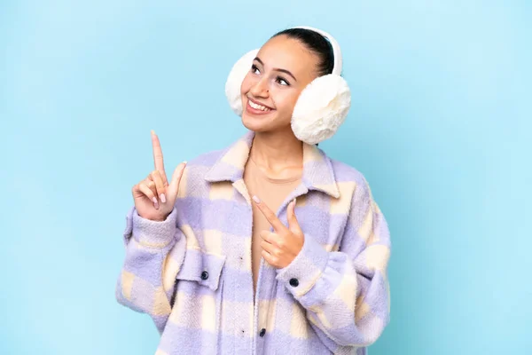 stock image Young Arab woman wearing winter muffs isolated on blue background pointing with the index finger a great idea