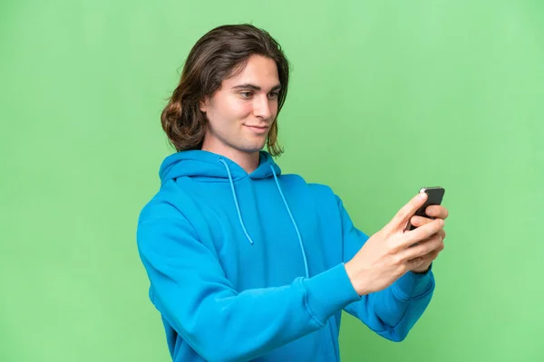 緑のクロマの背景に隔離された若いハンサムな男が携帯電話でメッセージや電子メールを送信します — ストック写真
